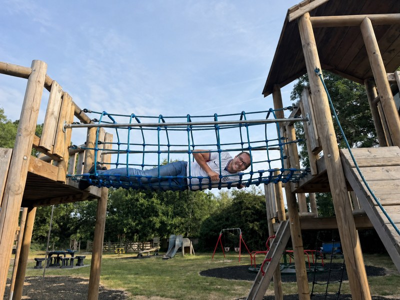 Scott lying inside a rope bridge on a wooden playground